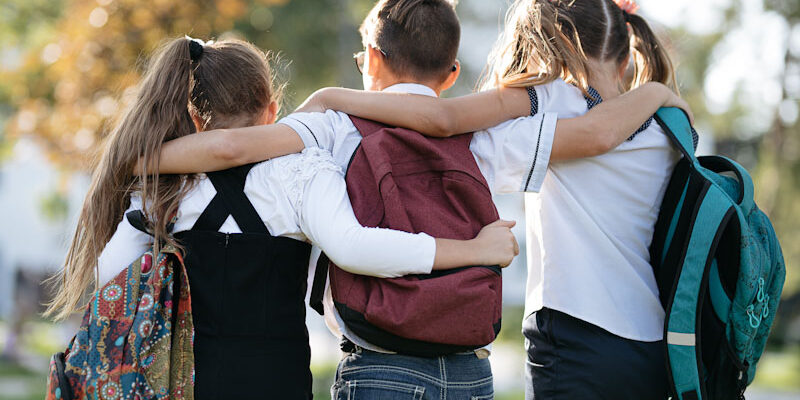 school friends a boy and two girls with school backpacks on thei